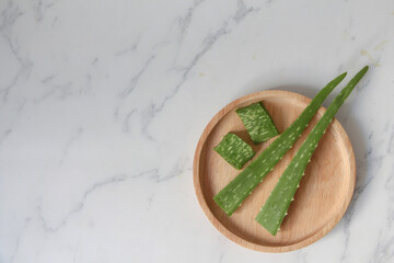 Top view Fresh Aloe vera leaves in wooden bowl. on white marble background. hair care and skin care concept. copy space.