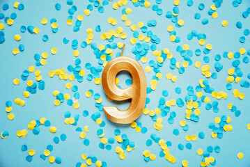 Number 9 nine golden celebration birthday candle on yellow and blue confetti Background. nine years birthday. concept of celebrating birthday, anniversary, important date, holiday