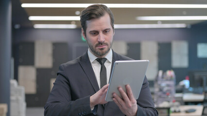 Portrait of Businessman Browsing Internet on Tablet in Office
