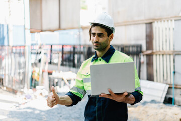 Construction engineers wear safety hardhat and in vest use a laptop computer on building site