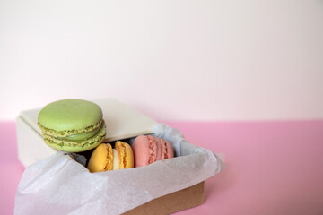 Cardboard box with three macarons inside, green, pink and blue, on a pink background. Concept of sweet temptation, caprice, gift. Copy space