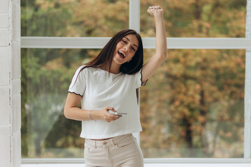 Happy young woman in earphones is listening to music with smartphone, dancing and smiling