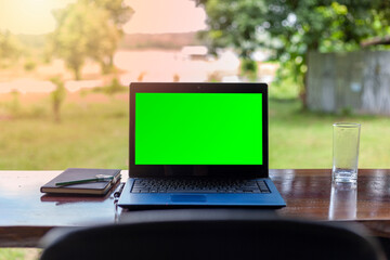 Fototapeta premium Green screen notebook with notebooks placed on a wooden table against a beautiful natural scenery background.
