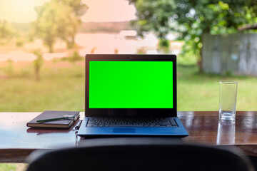 Green screen notebook with notebooks placed on a wooden table against a beautiful natural scenery background.