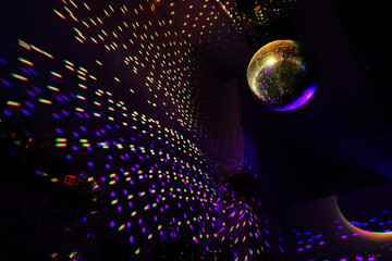 A large disco ball reflects the light of yellow, and purple colors in a dark hall for discos.  - obrazy, fototapety, plakaty