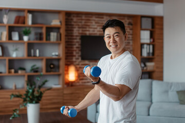 Healthy lifestyle, sports at home concept. Happy asian mature man lifting dumbbells, exercising in living room interior