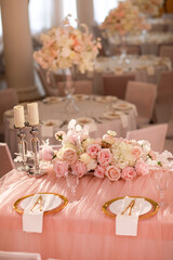 table decoration with pink tablecloth, crystal candlesticks with candles and white pink flowers in restaurant . stylish wedding day. setting table with gold plate, fork and knife