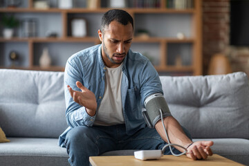 Sick Black Man Measuring Arterial Tension While Sitting On Couch At Home