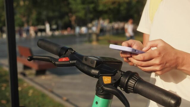 Student takes electric scooter or bicycle in a parking split, uses tourist phone app. Woman citizen using app on smartphone to unlock electric scooter on the street.