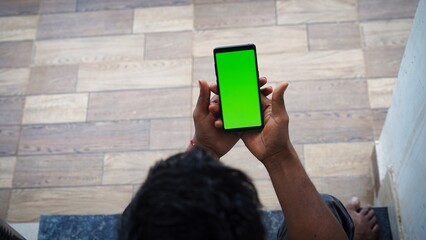 Man's hand shows mobile smartphone with green screen in vertical position isolated on tiles background. Mock up mobile