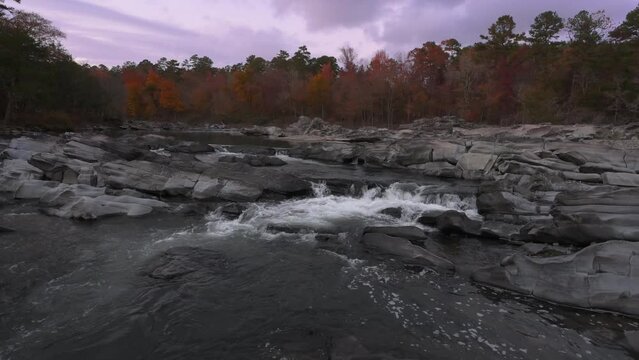 Purple sunset over fall forest at Cossatot Falls state park Arkansas as river rapids flow river unique rocky boulders 