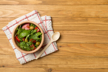 Fresh salad with arugula, spinach and vegetables on wooden background, top view
