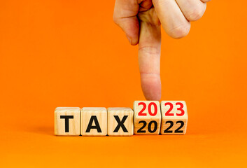 2023 tax new year symbol. Businessman turns a wooden cube and changes words Tax 2022 to Tax 2023. Beautiful orange table orange background, copy space. Business 2023 tax new year concept. - obrazy, fototapety, plakaty