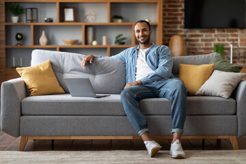 Obraz premium Handsome Black Man Sitting On Couch With Laptop And Smiling At Camera