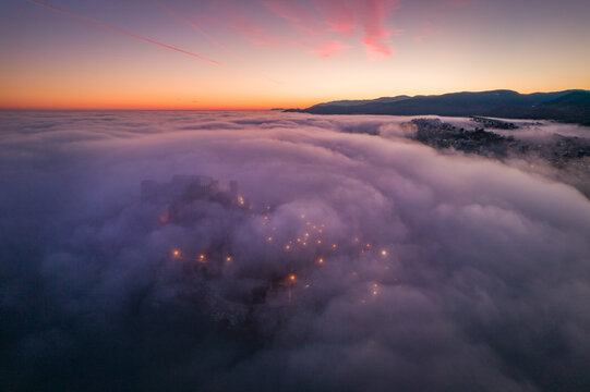 Fotografía aérea del castillo de Peñíscola sumido en la niebla al anochecer con colores en el cielo.
