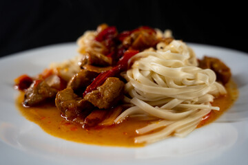 the lagman dish. a white plate. pieces of meat. pieces of vegetables. dark background