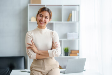 Picture of a charming, beautiful Asian businesswoman standing with her arms crossed and smiling and happily looking at the camera in her office.