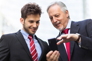 Senior manager showing something on a smartphone to his younger colleague