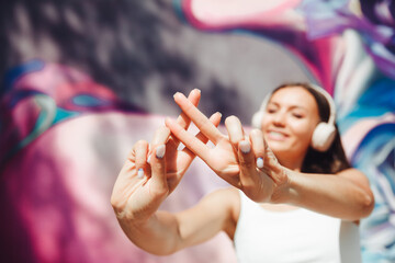 the girl makes a hashtag with her hands. a young woman wearing headphones shows a hashtag against the background of the street and graffiti - obrazy, fototapety, plakaty