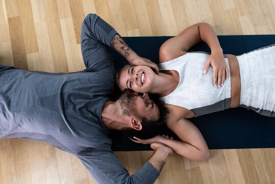 Young happy married couple man and woman lying on the floor on yoga mats after home workout training. Positive active people in their apartment sweaty after exercising.