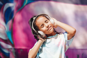 Happy childhood. A happy little girl listens to music and dances in the street. A small child wearing headphones. spring and autumn fashion. favorite music in headphones. generation z