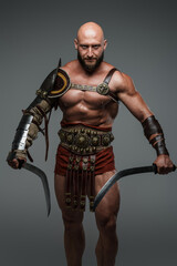 Portrait of ancient gladiator dressed in armour holding swords isolated on gray.