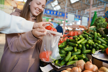 Shot of glad couple of man and woman byuing fresh peppers in vegetable store in bazaar.