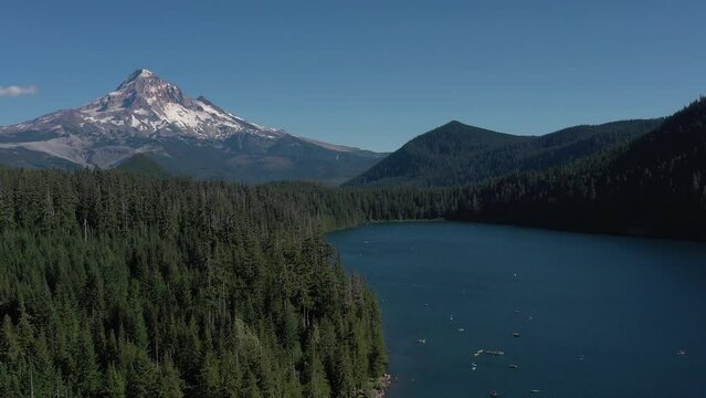 Aerial orbit and reveal shot of Mt. Hood and many boats and kayaks on water at Lost Lake during the peak of summer season in Oregon.