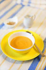 Pumpkin soup, mashed cream soup on a yellow platter with a spoon.
