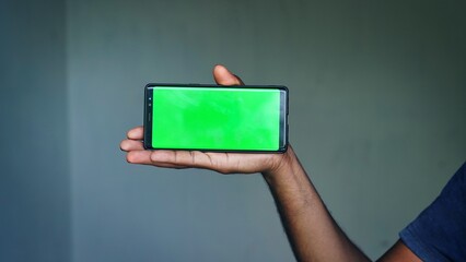 Man's hand shows mobile smartphone with green screen in vertical position isolated on lite blue background. Mock up mobile