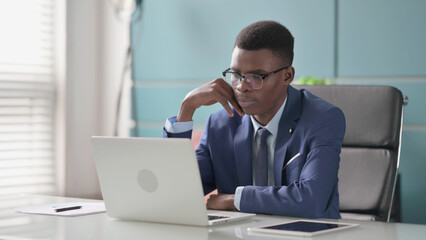 Young African Businessman Thinking while Working on Laptop in Office