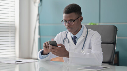 Fototapeta na wymiar Young African Doctor using Smartphone in Office