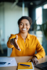 Cooperation concept. Happy black businesswoman extending hand for handshake at camera, sitting at desk in office