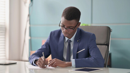Fototapeta premium Young African Businessman Writing on Paper in Office