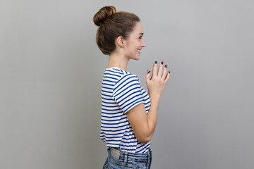 Side view portrait of cunning devious woman wearing striped T-shirt clasping hands and smirking...