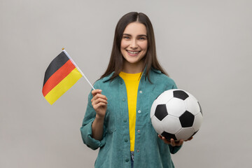 Smiling satisfied woman holding in hands flag of Germany and football ball, supporting favourite...