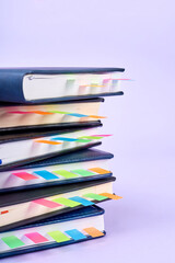 Close-up of a stack of office notepads with colorful sticky page markers sandwiched between pages on purple background