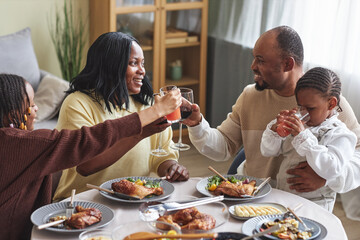 Happy parents toasting with drinks together with children at dining table in living room