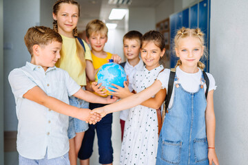 Teamwork concept. Group of five different age kids play globe ball in teamwork in school corridor...