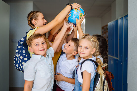 Different age team of children playing with globe in hallway at school. . Education, ecology, creativity and logical thinking concept.