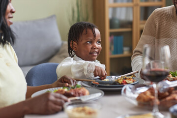 African little girl sitting at table and having dinner together with her family at home