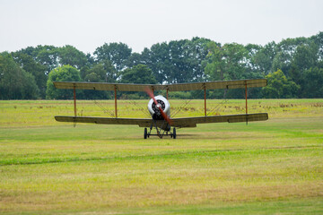 Vintage biplane prepares for takeoff at an open airfield surrounded by lush greenery on a clear day © Strikernia