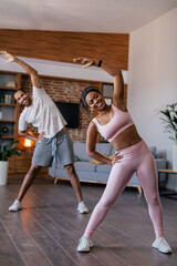 Obraz premium Cheerful young african american husband and wife in sportswear doing stretching or warm up exercises