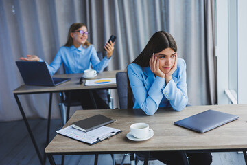 A European businesswoman is talking on a mobile phone while her European colleague is working in the background. Concept of modern successful women. Young girls sitting at desks in sunny office