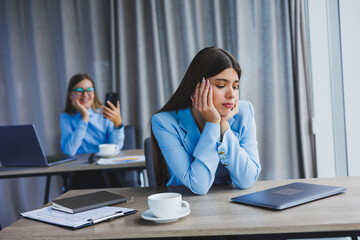 A European businesswoman is talking on a mobile phone while her European colleague is working in the background. Concept of modern successful women. Young girls sitting at desks in sunny office