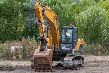 Yellow crawler excavator at a construction site next to a forest