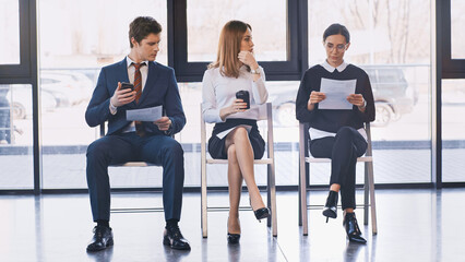 job seekers with resumes sitting near woman with takeaway drink in office.
