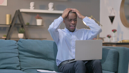 African Man with Laptop Reacting to Loss on Documents, Sofa