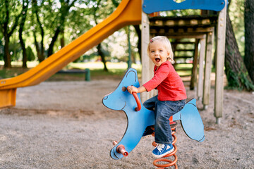Little girl sits laughing on a spring swing balancer. High quality photo