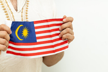 Malay, wearing a traditional shirt, holds the Malaysian flag in front of him